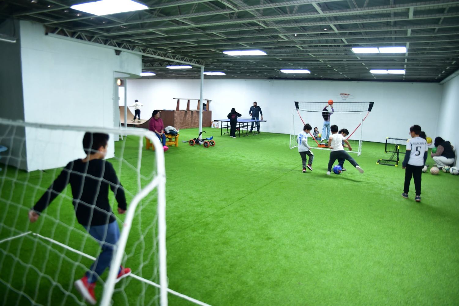 Cancha de fútbol techada con niños jugando, mesa de ping pong y aro de básquetbol