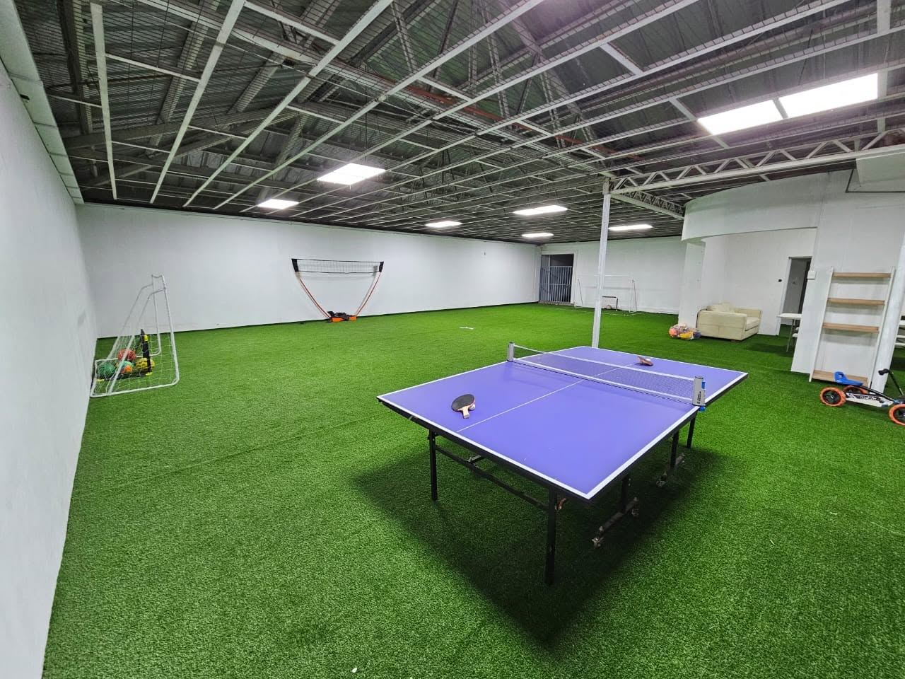 Mesa de ping pong sobre pasto sintético con arcos de fútbol al fondo